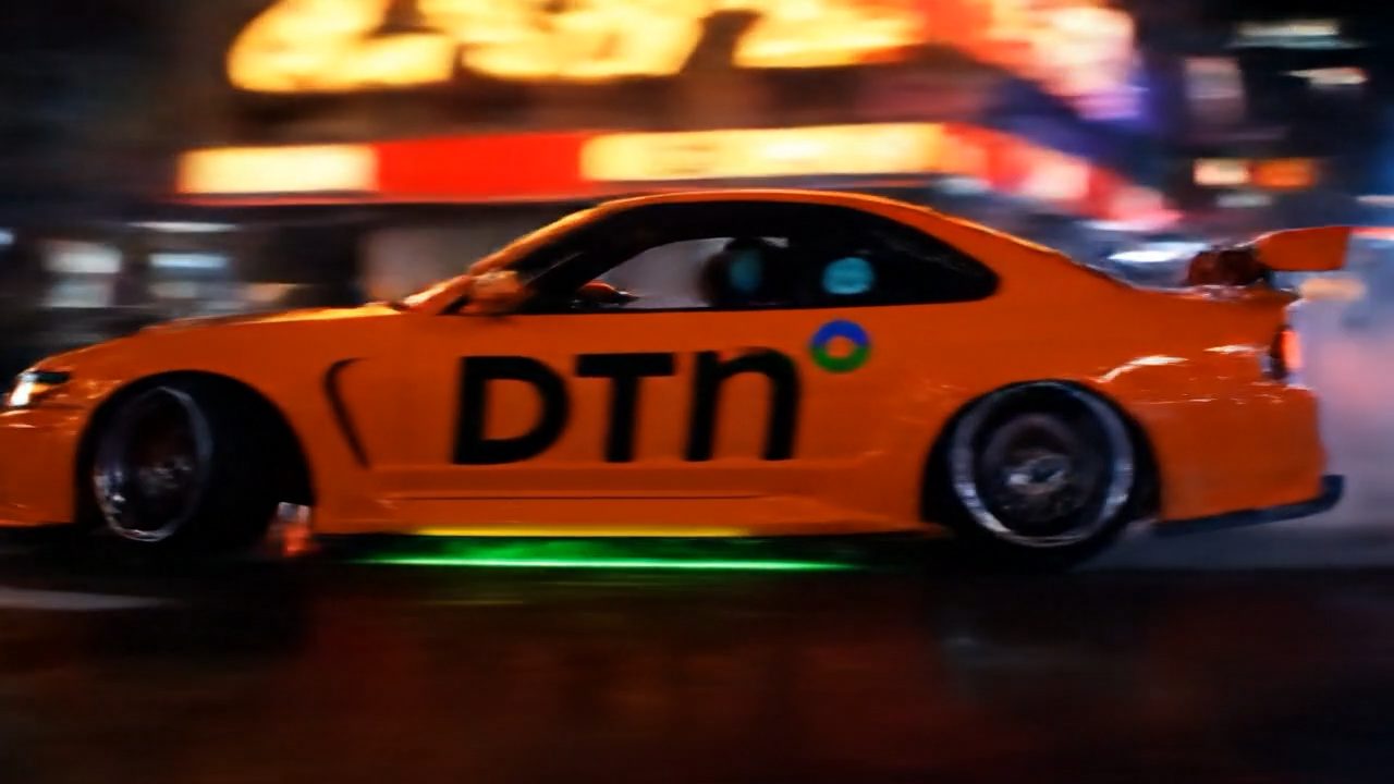 An orange drift car in DTN livery sliding through a neon-lit street at night, motion blurred.
